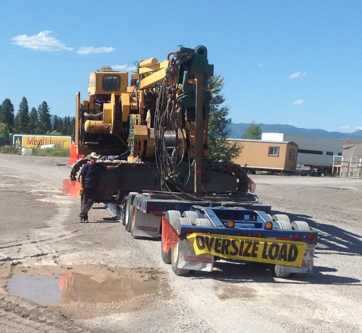 Track drill rig secured on a lowboy trailer with oversize load banner