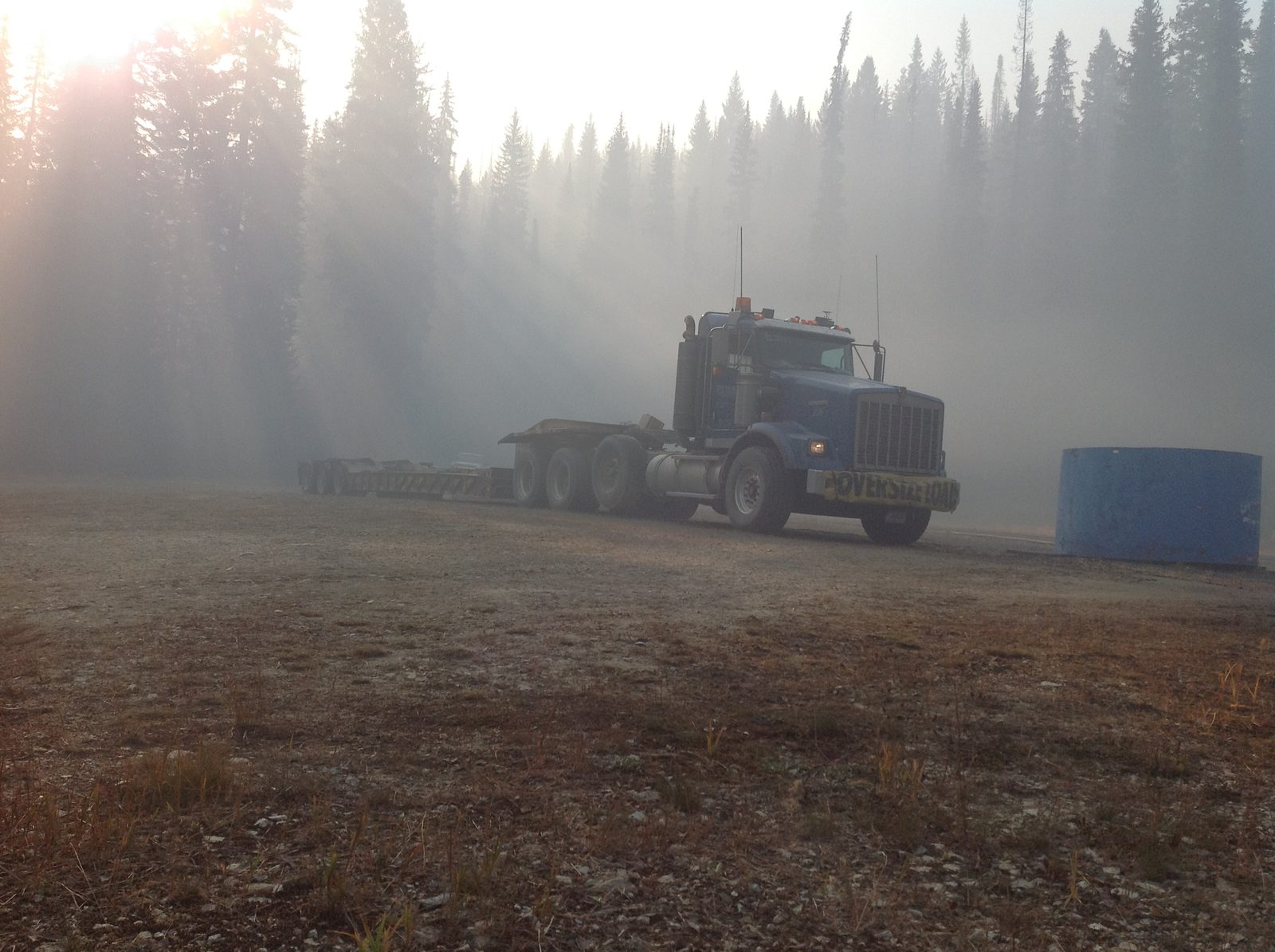 Heavy haul tractor and lowboy trailer in dense wildfire smoke in a forest clearing